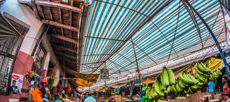 A photo showing an outdoor market in Lamu, Kenya. There are several stalls selling fruit underneath a striped tarp roof.